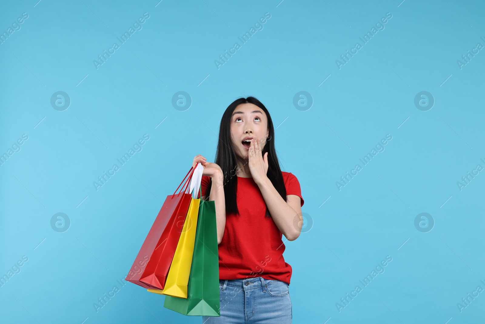 Photo of Surprised woman with shopping bags on light blue background