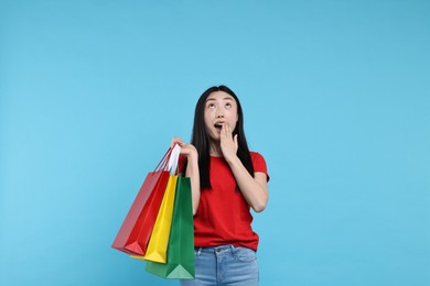 Surprised woman with shopping bags on light blue background