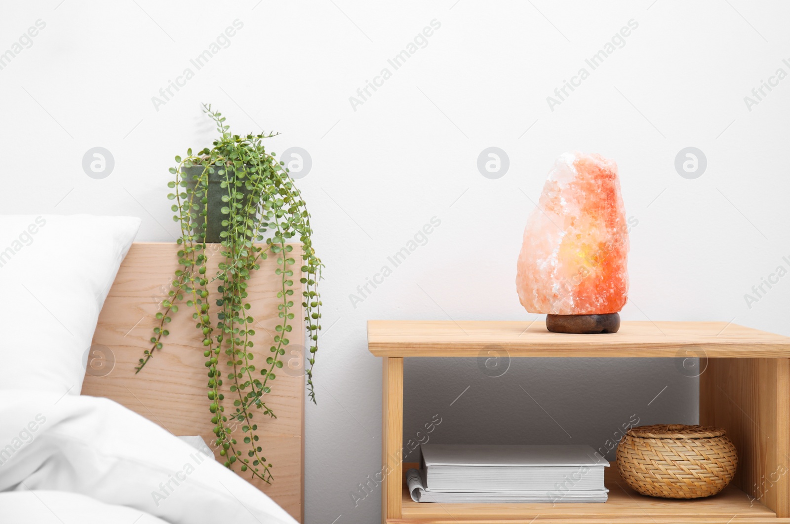 Photo of Himalayan salt lamp on wooden nightstand in bedroom