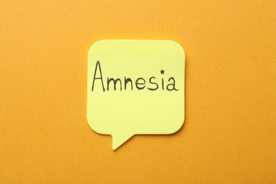 Photo of Yellow sticky note with word Amnesia on orange background, top view