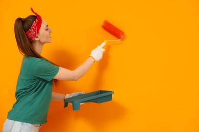 Designer painting orange wall with roller, space for text