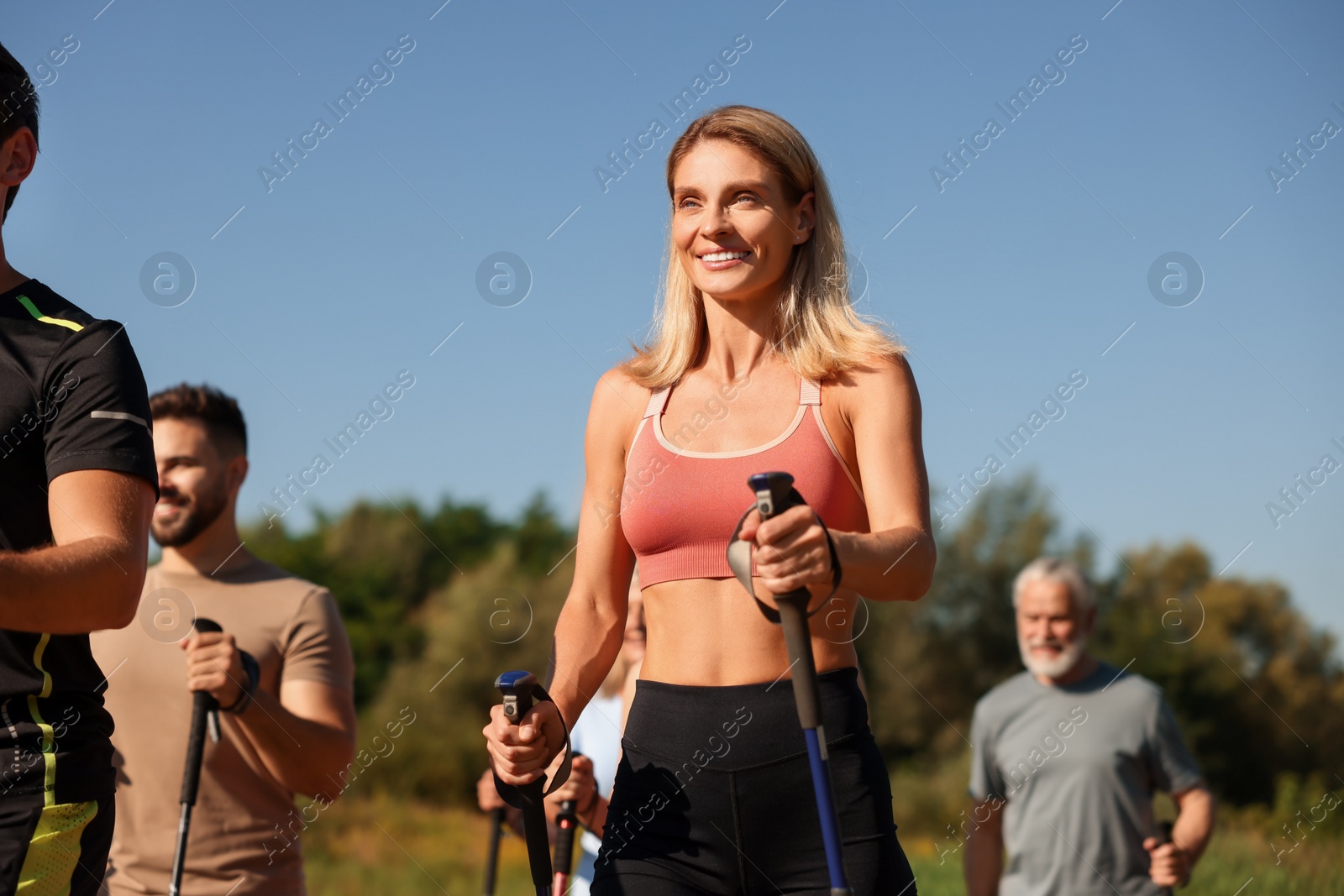 Photo of Group of happy people practicing Nordic walking with poles outdoors on sunny day