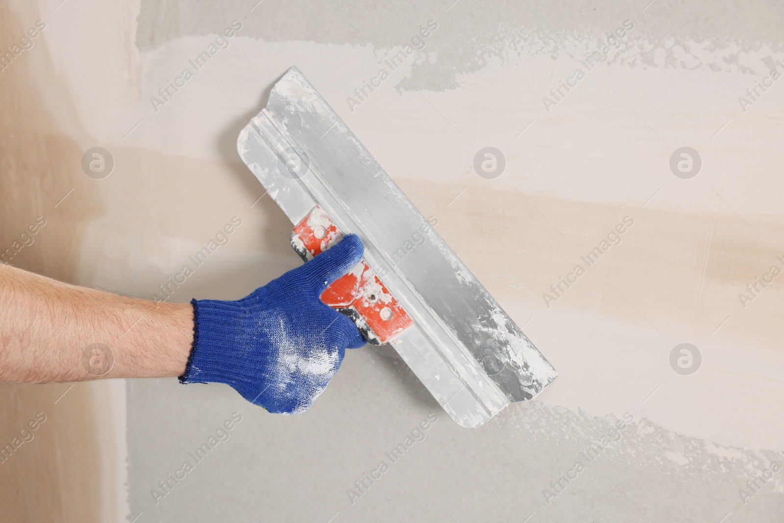 Photo of Worker plastering wall with putty knife indoors, closeup