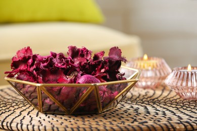 Photo of Aromatic potpourri of dried flowers in bowl and burning candles on wooden table indoors