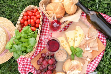 Photo of Picnic blanket with wine and food on green grass, top view