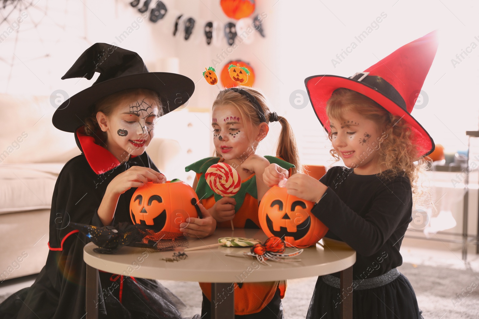 Photo of Cute little kids with pumpkin candy buckets wearing Halloween costumes at home