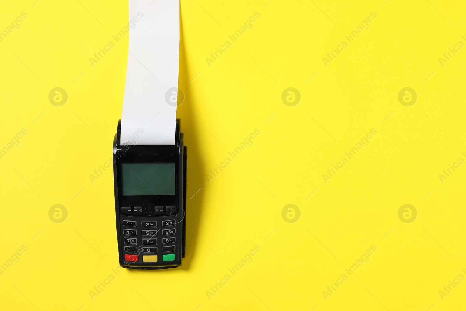 Photo of Payment terminal with thermal paper for receipt on yellow background, top view. Space for text