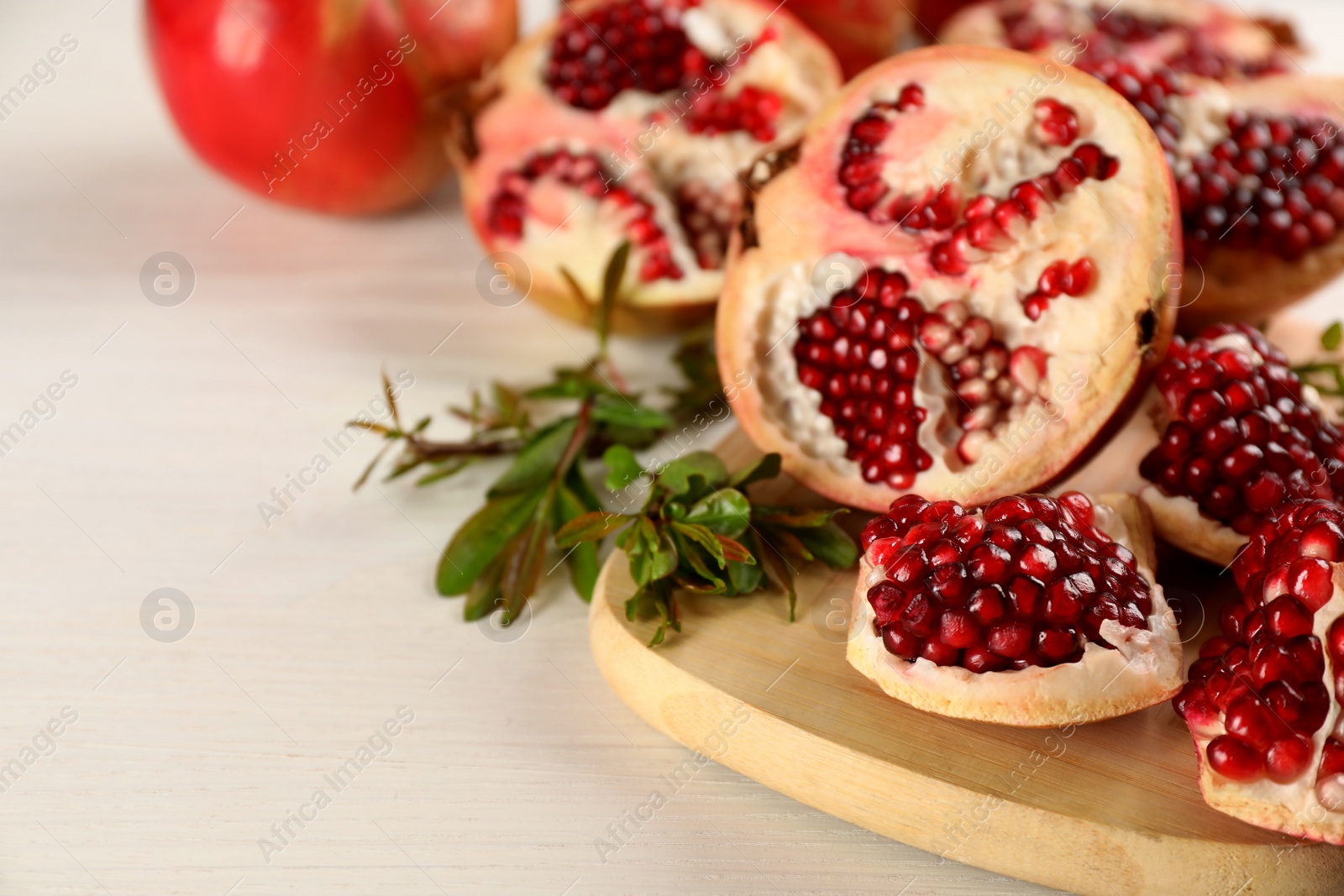 Photo of Delicious ripe pomegranates on white wooden table, closeup. Space for text