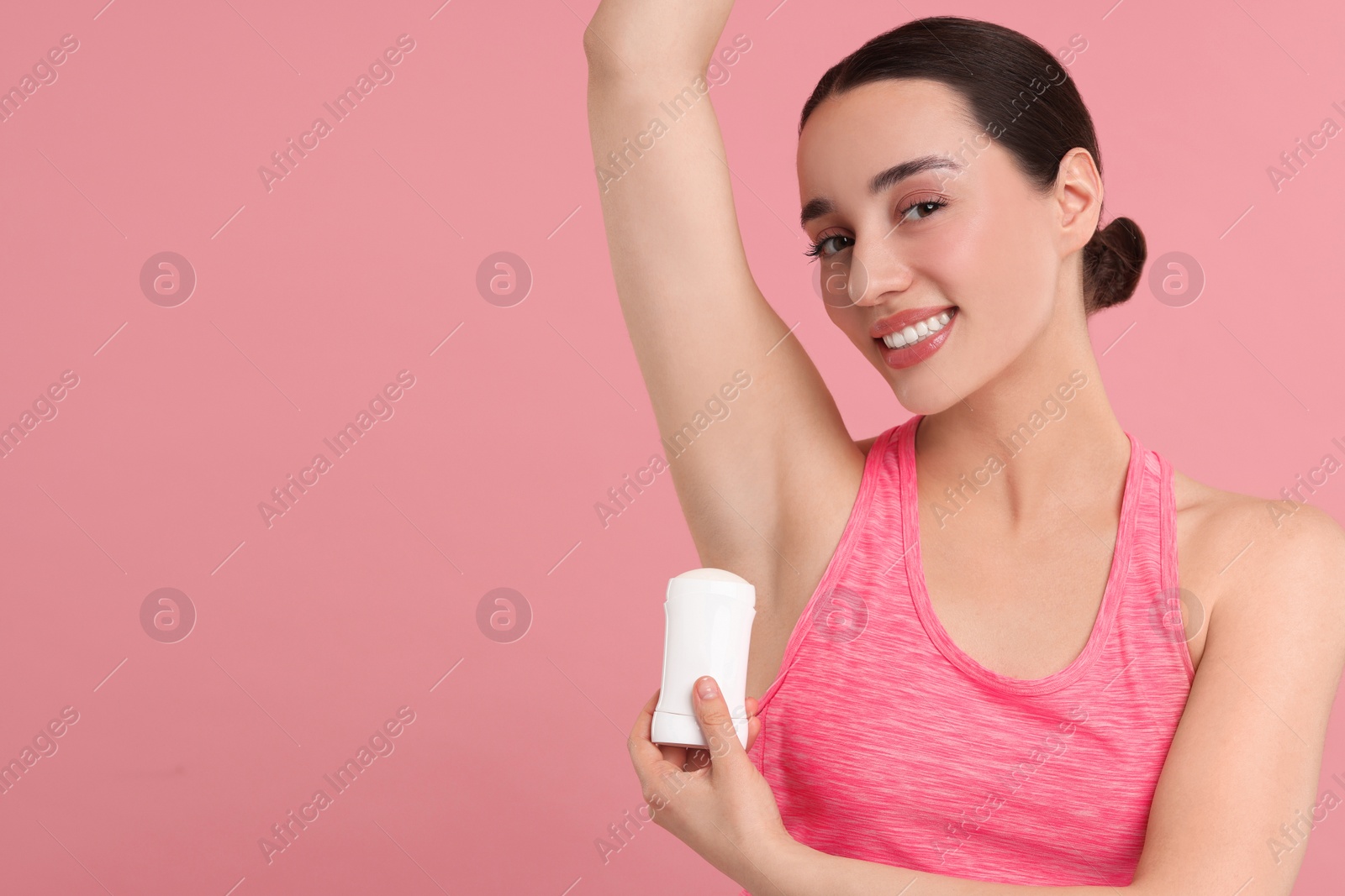 Photo of Beautiful woman applying deodorant on pink background, space for text