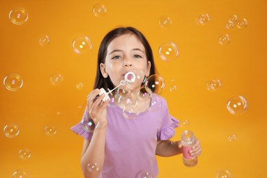 Little girl blowing soap bubbles on yellow background