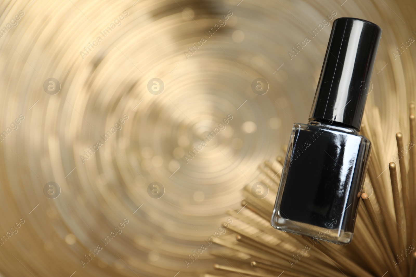 Photo of Stylish presentation of black nail polish in bottle on golden textured surface, closeup. Space for text