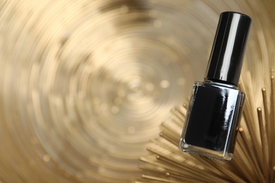 Photo of Stylish presentation of black nail polish in bottle on golden textured surface, closeup. Space for text