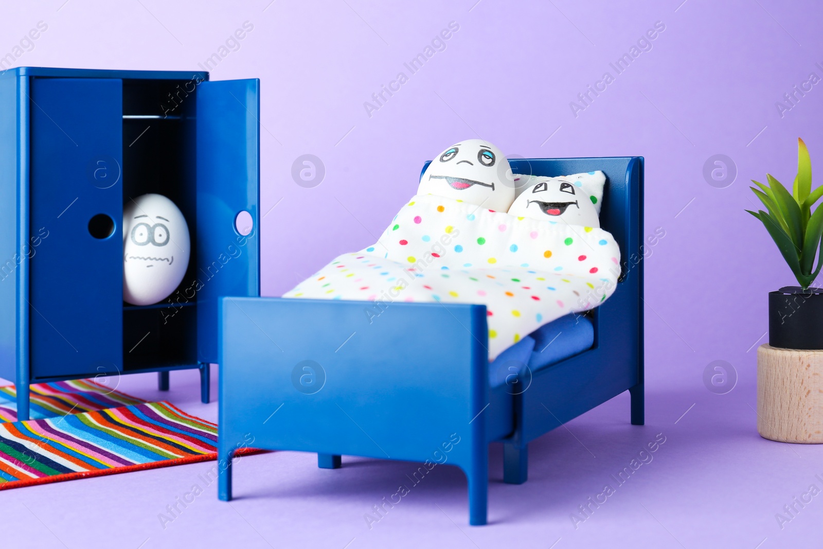 Photo of Small bed with couple of eggs and lover hiding in closet on lilac background