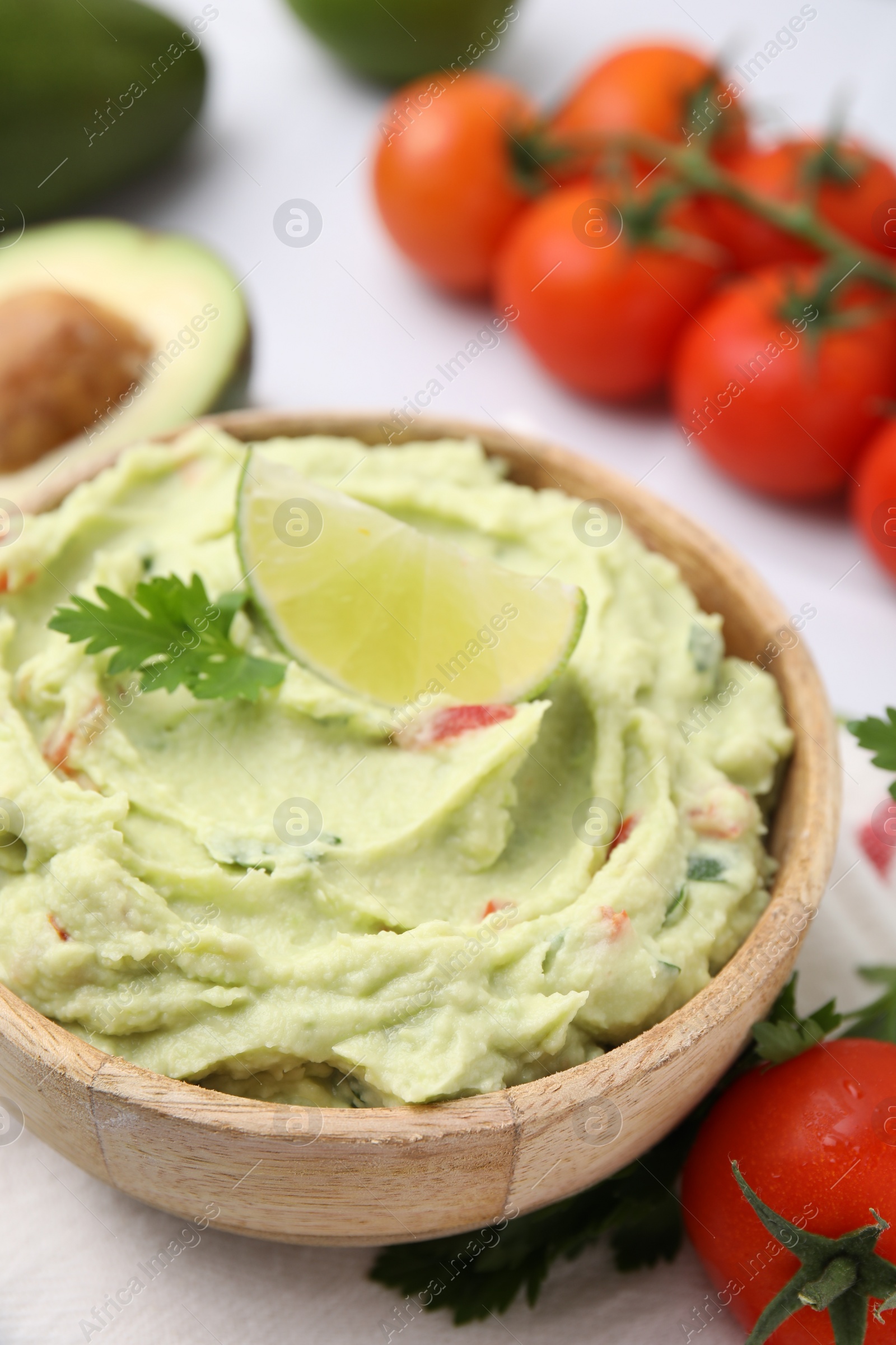 Photo of Bowl of delicious guacamole and ingredients on white table, closeup