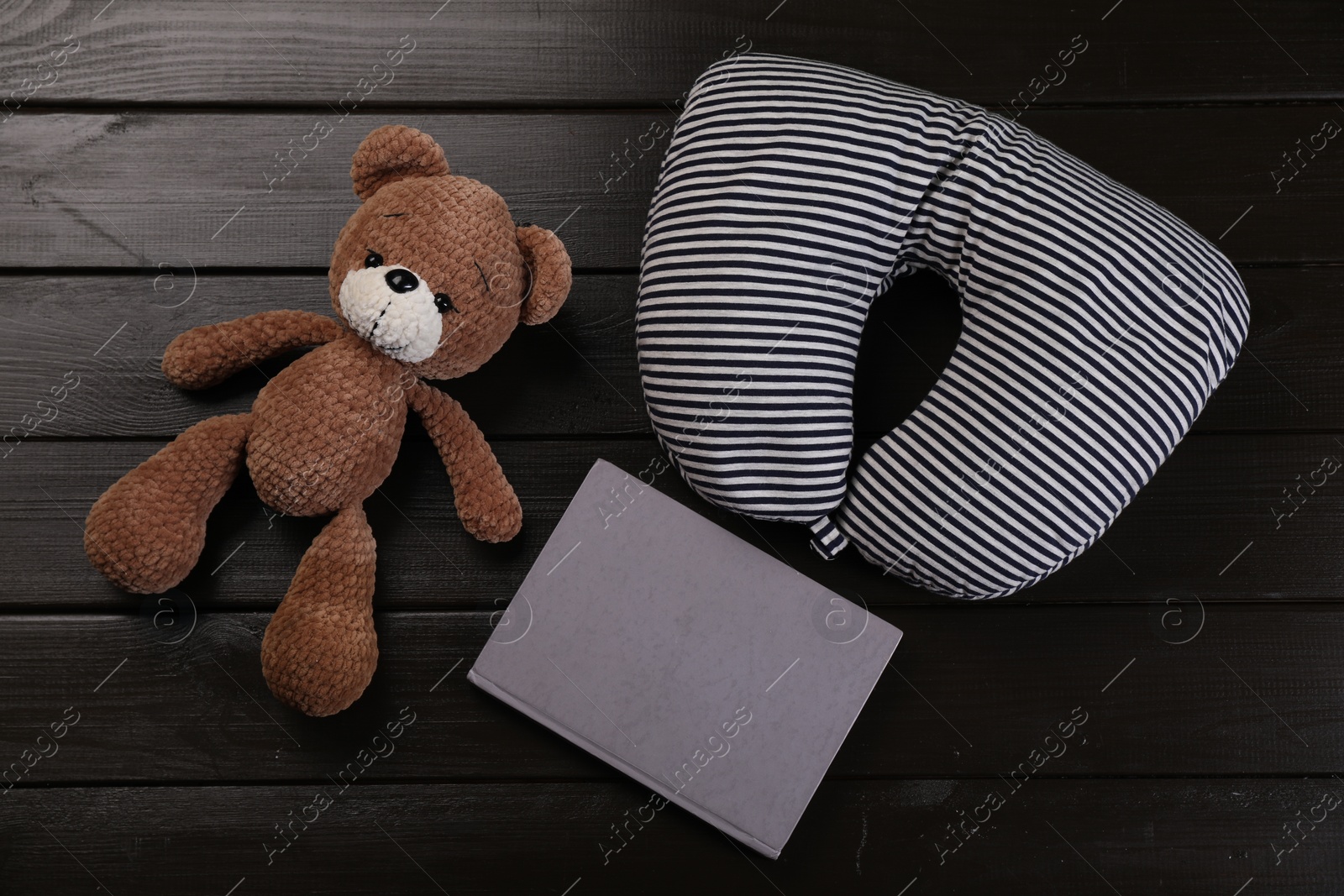 Photo of Striped travel pillow, notebook and toy bear on dark wooden background, flat lay