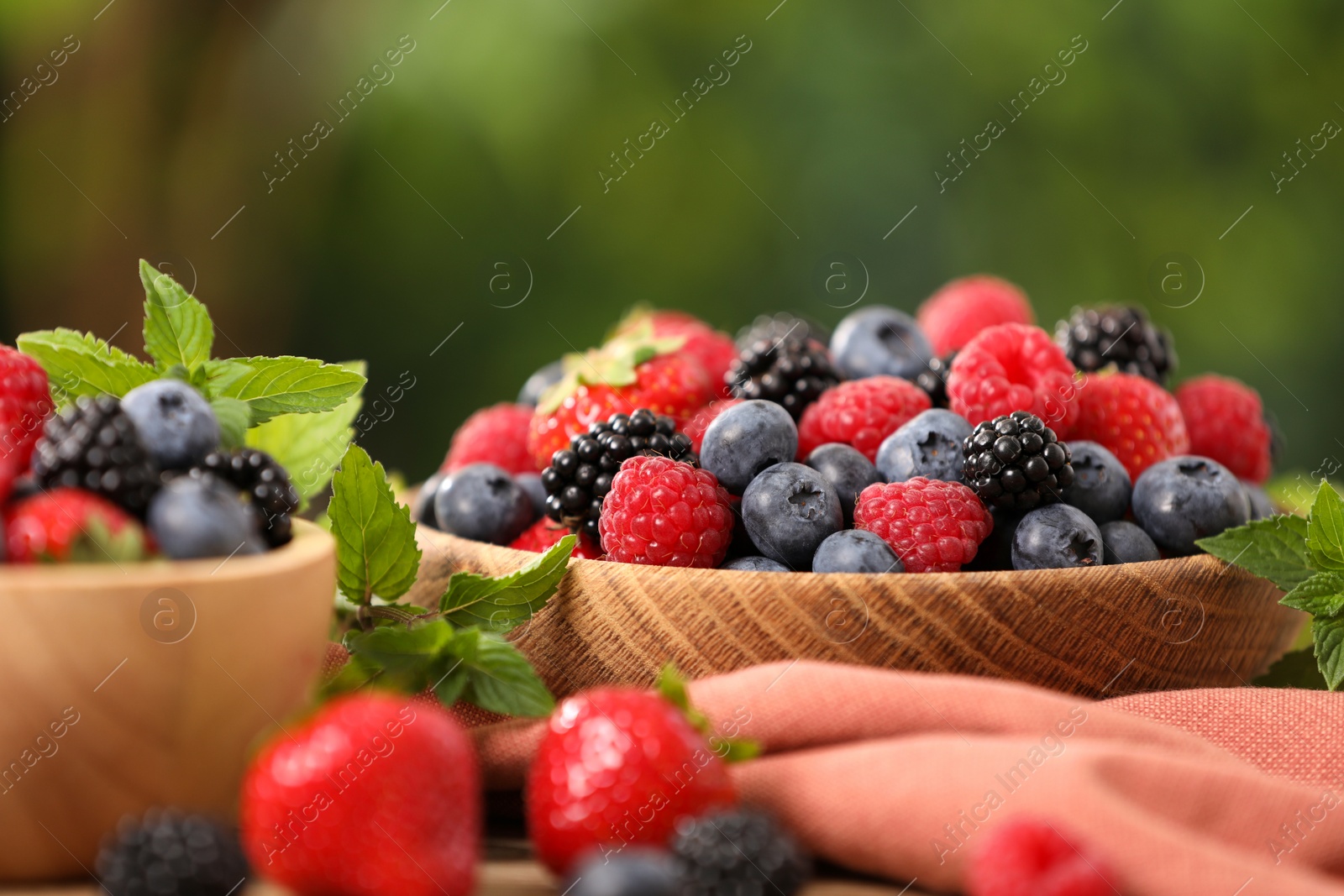 Photo of Bowls with different fresh ripe berries and mint on table outdoors, closeup