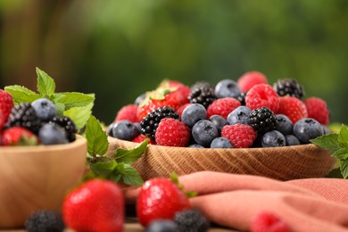 Bowls with different fresh ripe berries and mint on table outdoors, closeup