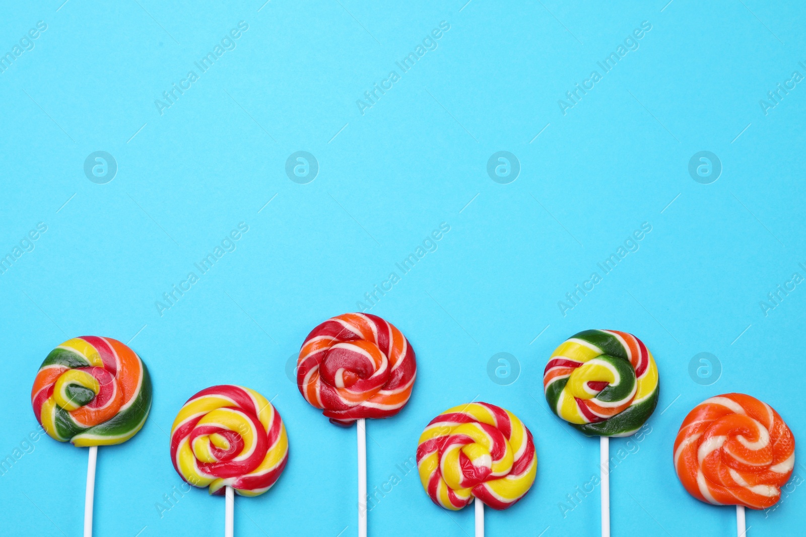 Photo of Sweet lollipops on light blue background, flat lay. Space for text