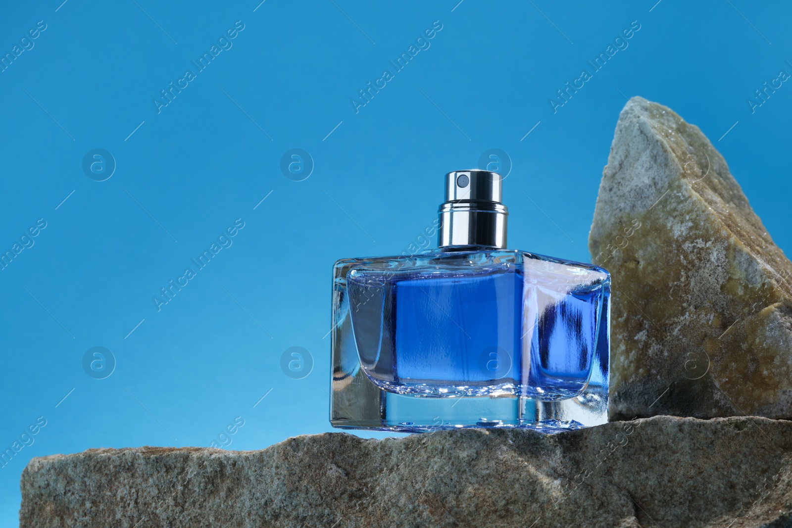 Photo of Stylish presentation of luxury men`s perfume on stones against light blue background. Space for text