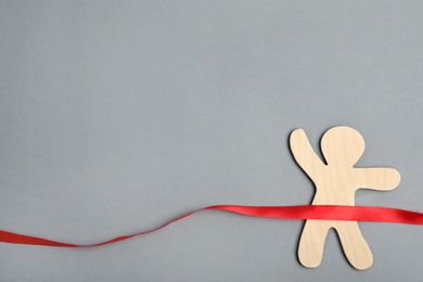Photo of Wooden man and red ribbon on grey background, top view with space for text. Victory concept