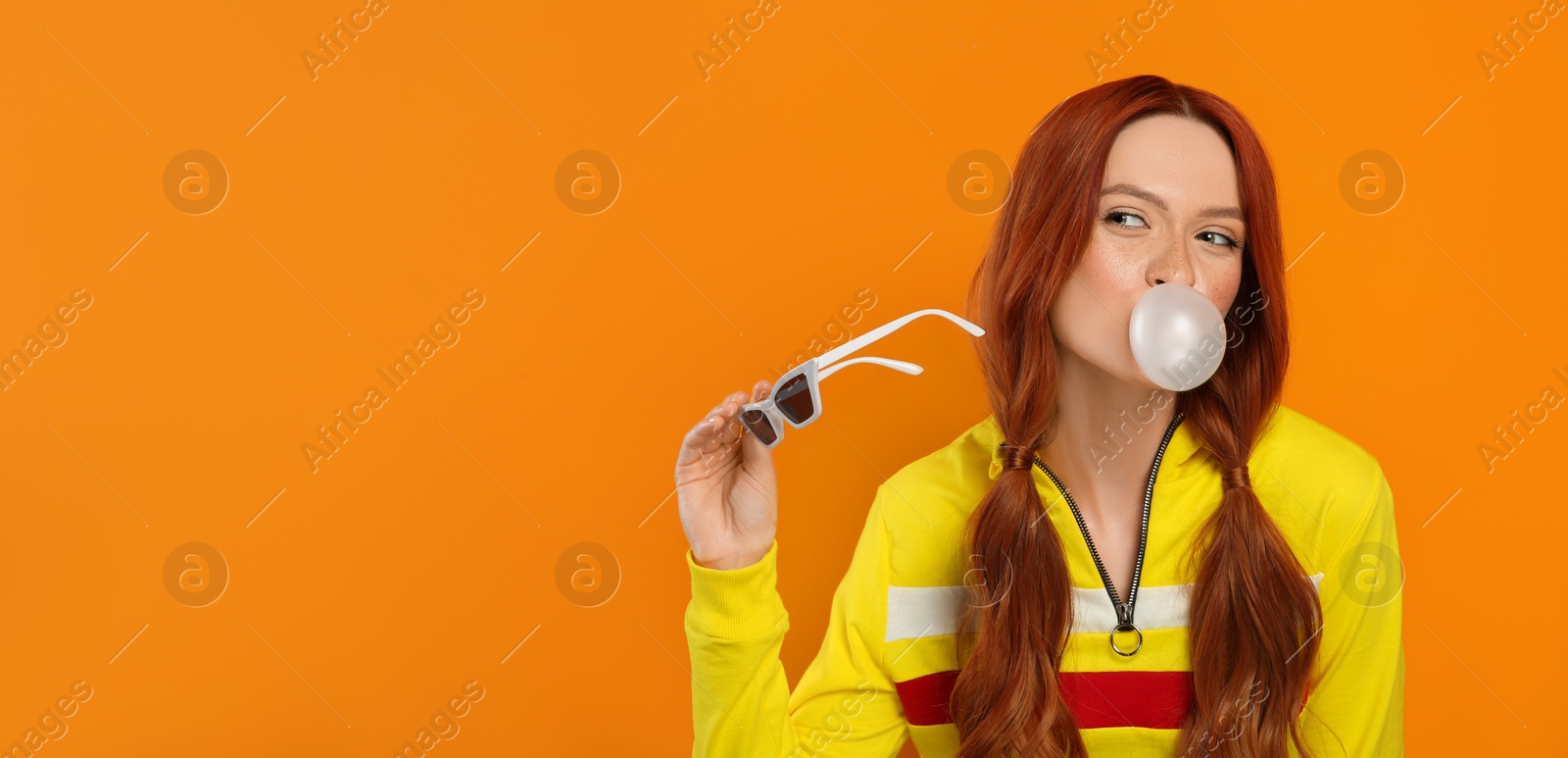 Photo of Beautiful woman blowing bubble gum on orange background