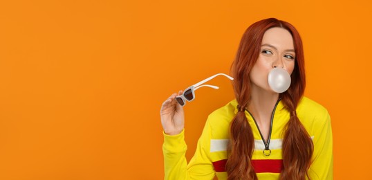 Beautiful woman blowing bubble gum on orange background