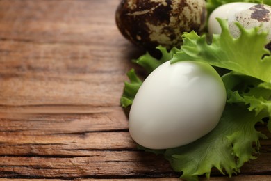Photo of Unpeeled and peeled boiled quail eggs with lettuce on wooden table, closeup. Space for text