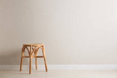 Stylish wooden stool near white wall, space for text. Interior element