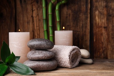 Photo of Stacked spa stones, bamboo, candles and towel on wooden table. Space for text