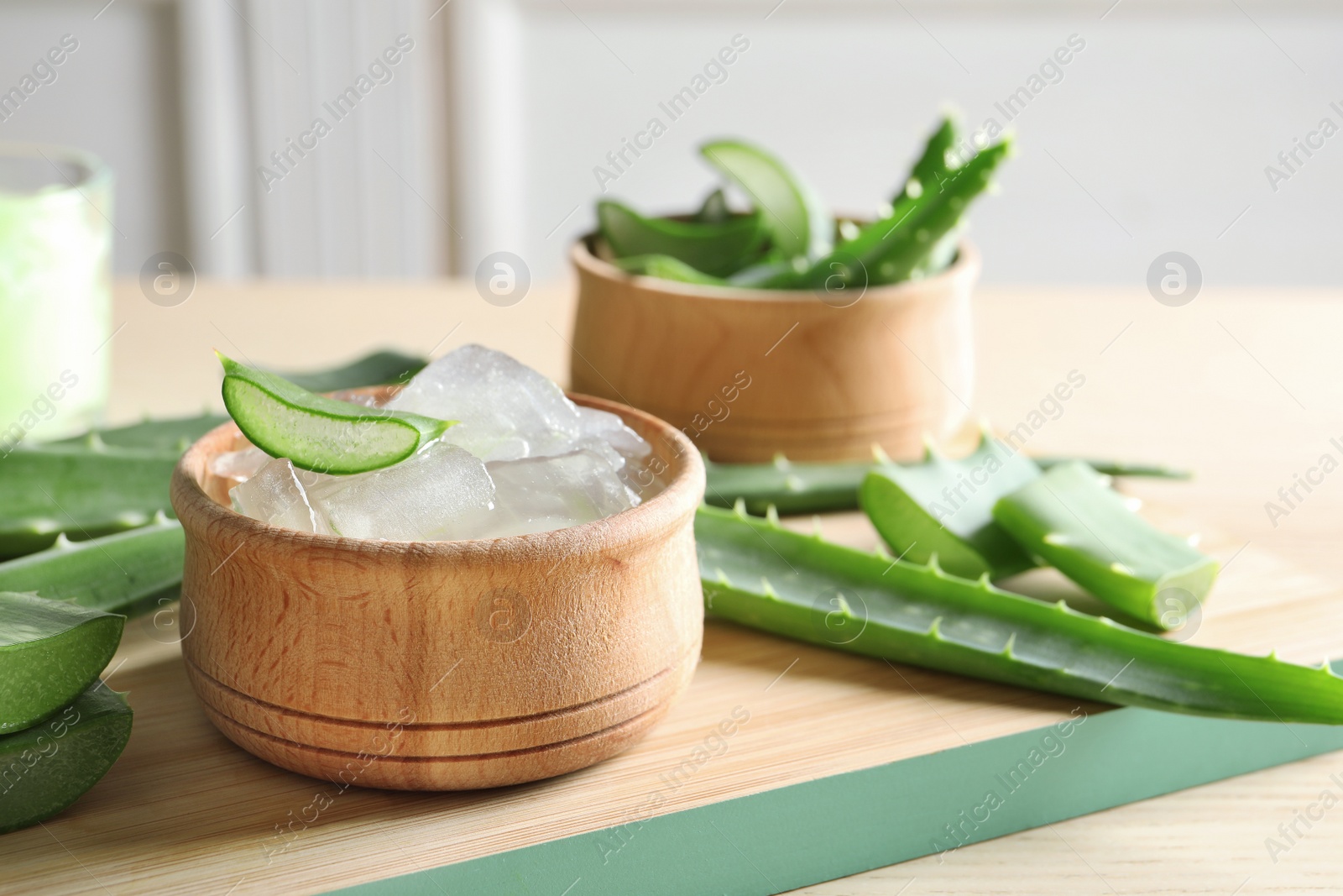 Photo of Bowl with peeled aloe vera and green leaves on wooden board