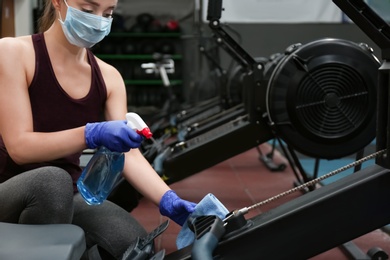 Photo of Woman cleaning exercise equipment with disinfectant spray and cloth in gym
