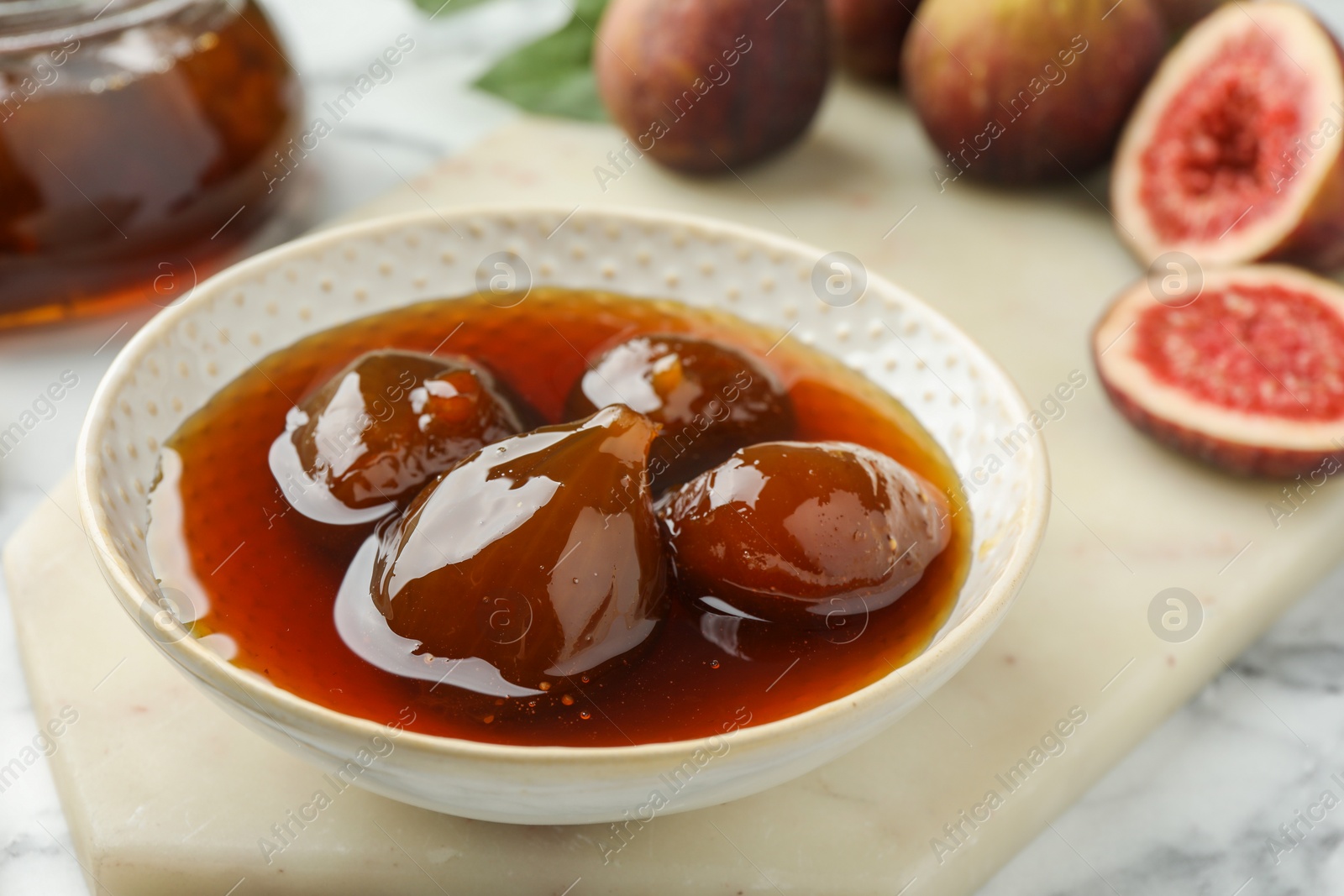 Photo of Bowl of tasty sweet jam and fresh figs on white marble table