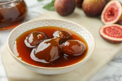 Bowl of tasty sweet jam and fresh figs on white marble table