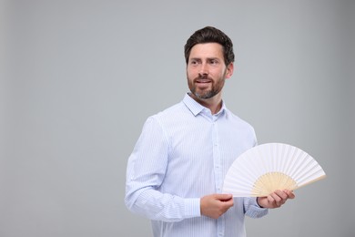 Photo of Happy man holding hand fan on light grey background. Space for text