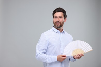 Happy man holding hand fan on light grey background. Space for text