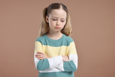 Portrait of sad girl with crossed arms on light brown background