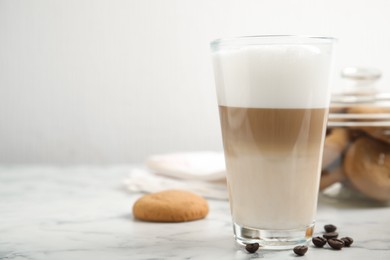 Photo of Delicious latte macchiato, cookies and coffee beans on white marble table, space for text