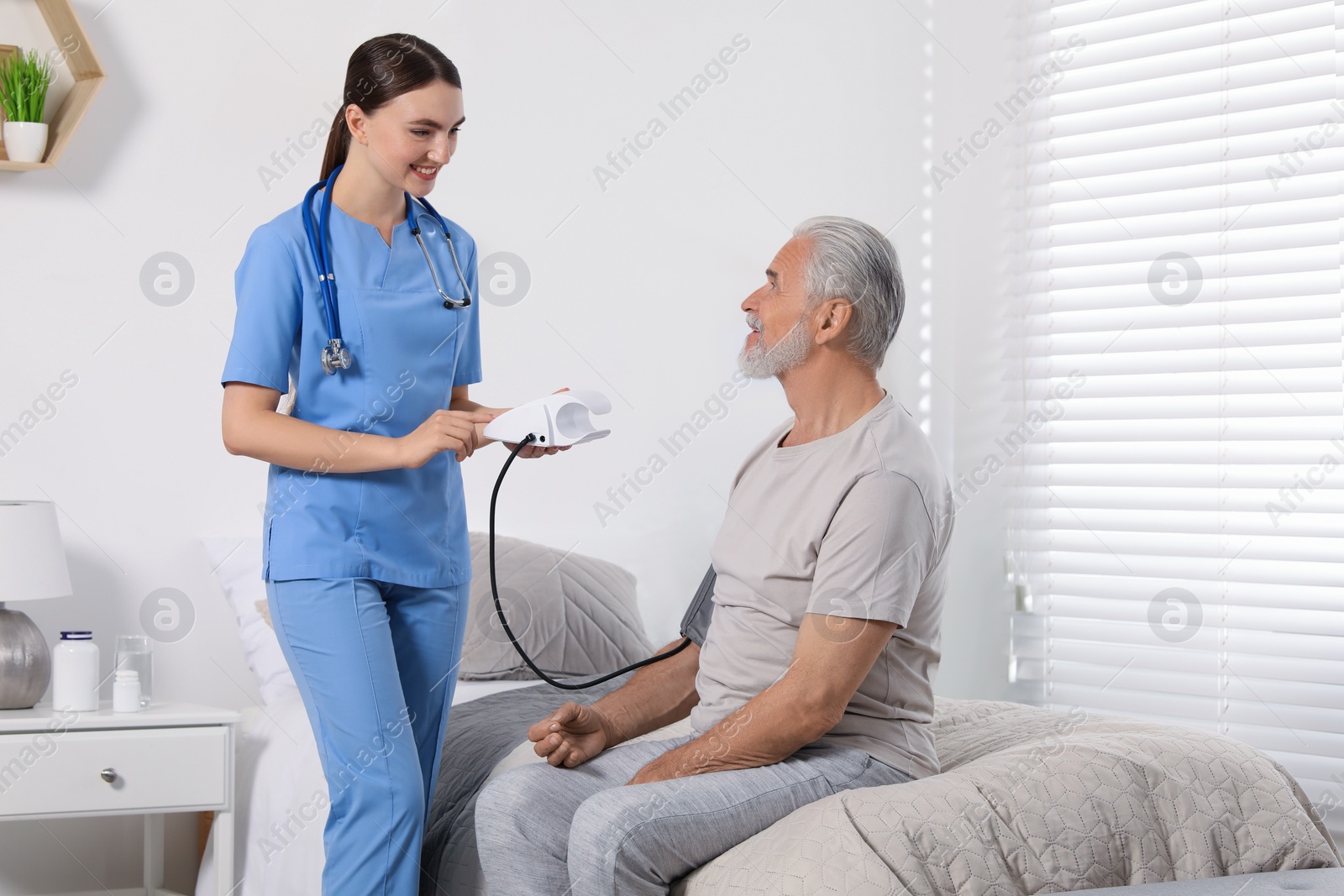 Photo of Young healthcare worker measuring senior man's blood pressure indoors