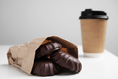 Photo of Delicious chocolate covered zephyrs in bag and paper cup on white table