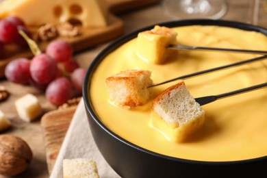 Photo of Tasty cheese fondue and forks with bread pieces on table, closeup