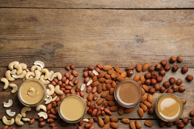 Photo of Jars with butters made of different nuts and ingredients on wooden table, flat lay. Space for text