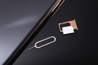 SIM card, smartphone and ejector on black background, above view