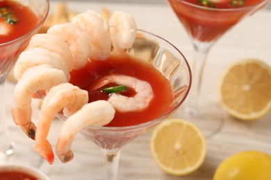 Photo of Tasty shrimp cocktail with sauce in glasses and lemon on table, closeup