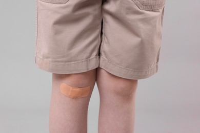 Photo of Little boy with sticking plaster on knee against light grey background, closeup