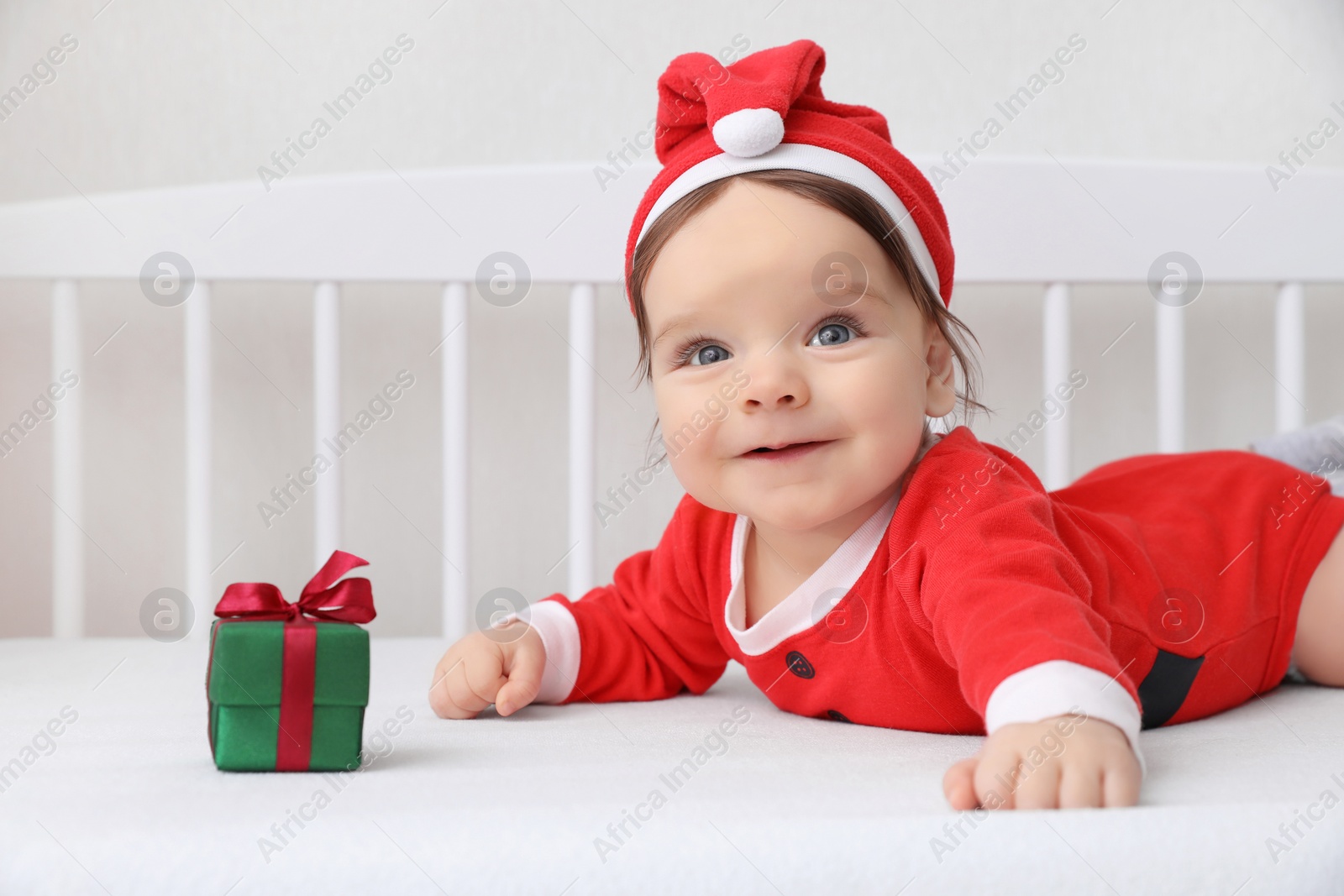 Photo of Cute baby wearing festive Christmas costume with gift box in crib