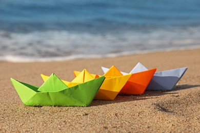 Bright colorful paper boats on sandy beach near sea