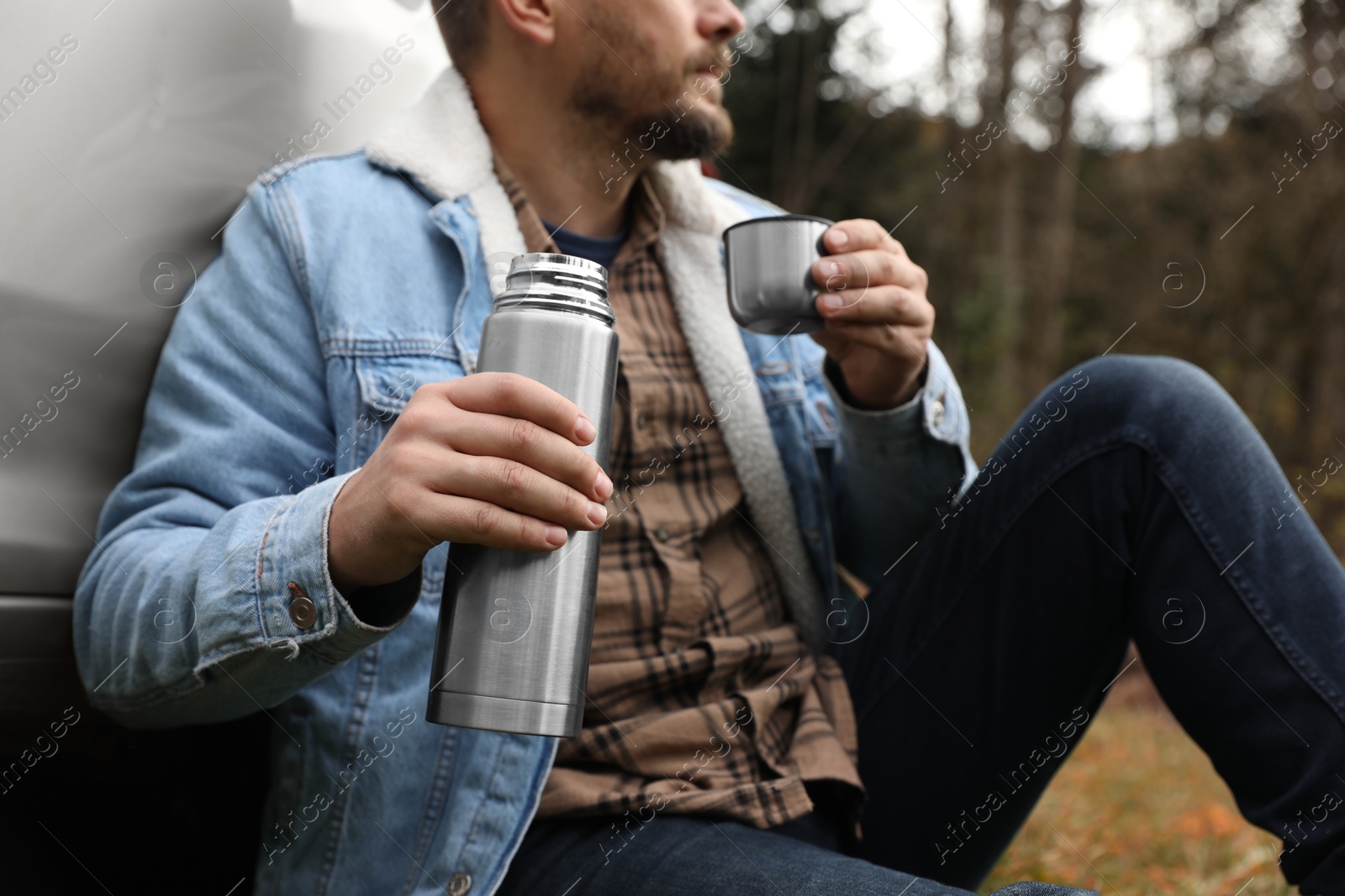 Photo of Man with metallic thermos and cup lid near car outdoors, closeup