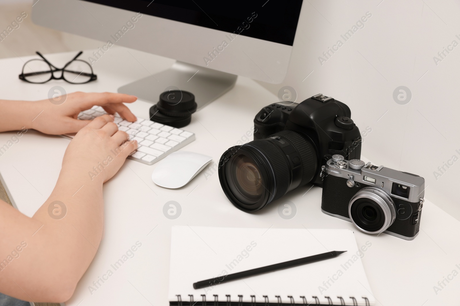 Photo of Photographer working on computer at white table with cameras indoors, closeup