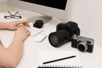 Photo of Photographer working on computer at white table with cameras indoors, closeup