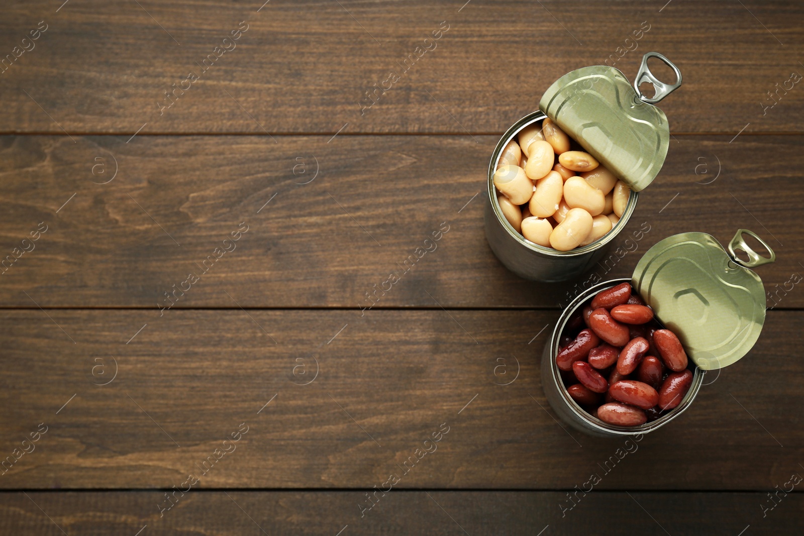 Photo of Tin cans with different canned kidney beans on wooden table, flat lay. Space for text